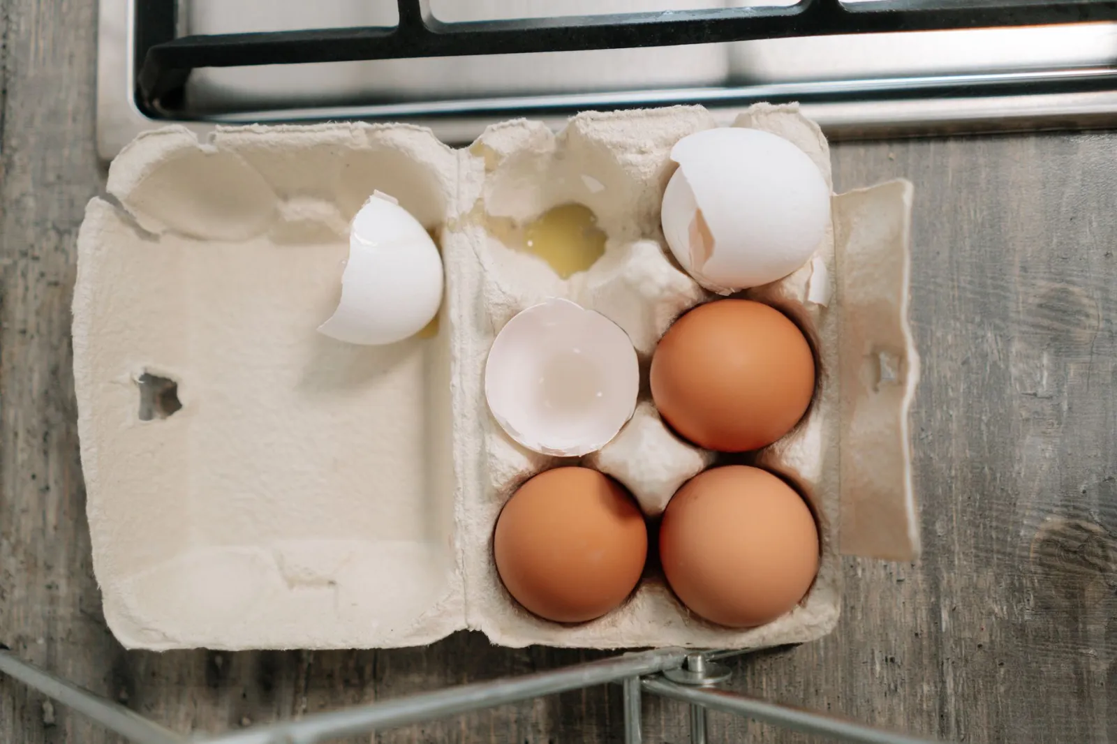 Overhead view of fresh brown and broken white eggs in carton on wooden surface.