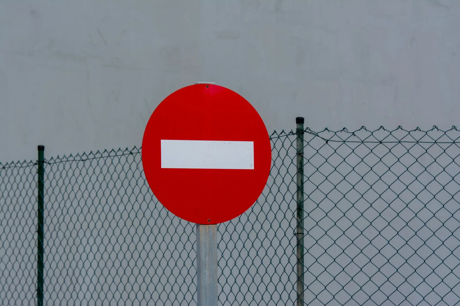 Red circular no entry sign in front of a mesh fence, symbolizing prohibition and security.